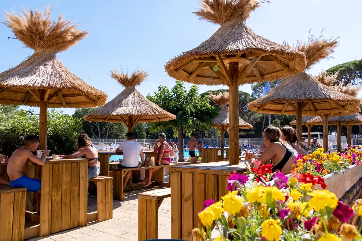 Paillotes et tables hautes du snack au bord des bassins