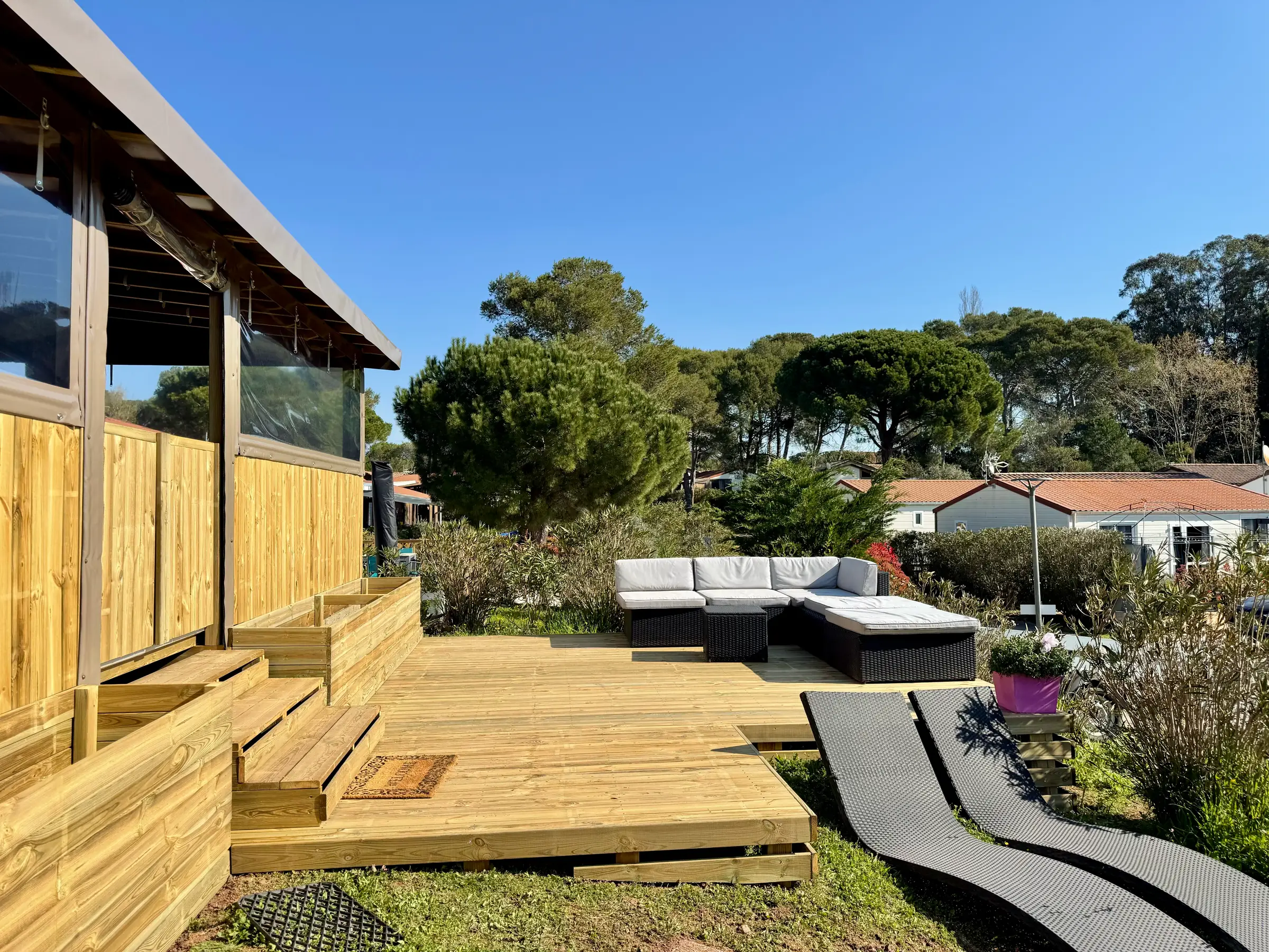 Deck en bois avec salon d'extérieur et bains de soleil, pins parasols en arrière-plan